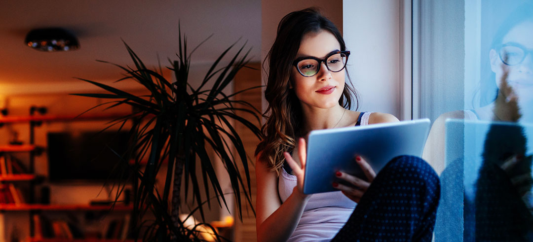 Mujer joven en el salón de su casa sujetando una tablet cerca de la ventana