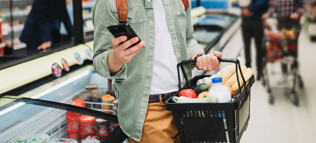 Persona en un supermercado mirando su smartphone mientras hace una compra semanal saludable