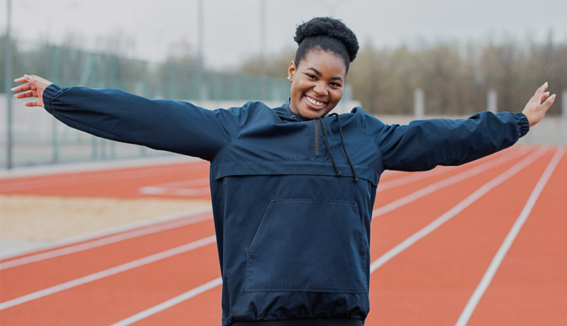 Mujer con los brazos abiertos con una pista de atletismo de fondo