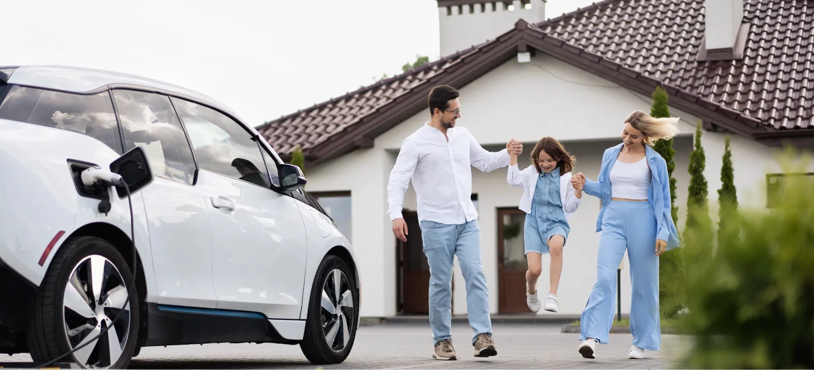 Familia feliz con un coche eléctrico cargando y su casa de fondo